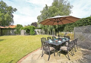 Eine Terrasse mit Esstisch und Stühlen, beschattet durch einen großen Sonnenschirm.