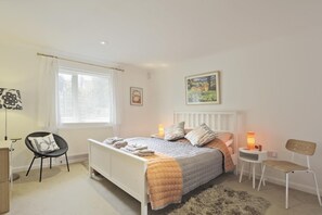 Ein Schlafzimmer mit Bett, Nachttischen, einem Sessel, einer Lampe, einem Heizkörper und einem Fenster mit Vorhängen.