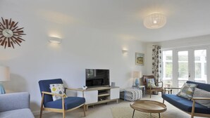 A modern living room with a flat-screen TV, two blue armchairs, a sofa, and a coffee table. - 5 Bed in Walberswick (oc-hferin) (Walberswick)