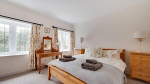 A bedroom with a bed, a wooden dresser, a mirror, two bedside tables with lamps, and a window with curtains. - 2 Bed in Walberswick (oc-hstone) (Walberswick)