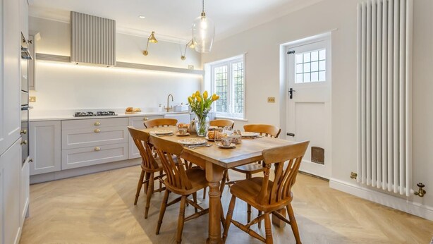 A modern kitchen with white cabinetry, a dining table set for four, and a large window with a view. - 2 Bed in Walberswick (oc-hstone) (Walberswick)