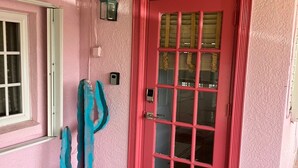 Pared exterior rosa con una puerta roja, una ventana y una escultura de cactus azul.