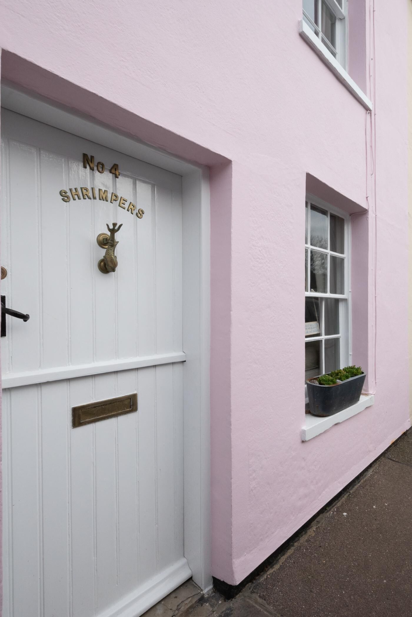 Un bâtiment rose avec une porte blanche portant l’inscription « No 4 SHRIMPERS���» et un heurtoir en laiton.
