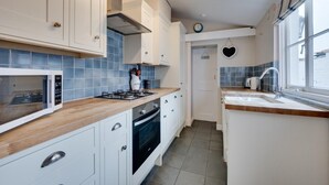 Een moderne keuken met witte kasten, een houten aanrecht, een ingebouwde oven, een magnetron en een spoelbak met een raam erboven.