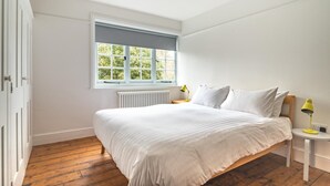 Ein Schlafzimmer mit einem großen Bett, einem Fenster, einer Heizung und einem Nachttisch mit Lampe.