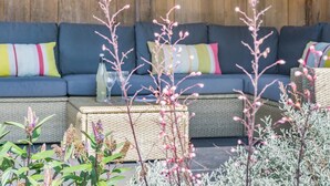 A sectional sofa with colorful cushions, a wicker coffee table, and various plants in a cozy outdoor seating area. - 4 Bed in Walberswick (oc-hwfern) (Walberswick)
