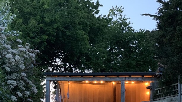 A wooden pergola with string lights, a stone wall, and a garden with various plants and flowers. - 4 Bed in Walberswick (oc-hwfern) (Walberswick)
