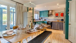 A modern kitchen with teal cabinets, a dining area with a wooden table set for four, and a bench. - 4 Bed in Walberswick (oc-hwfern) (Walberswick)