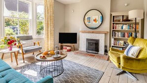 A living room with a fireplace, a television, and a bookshelf. - 4 Bed in Walberswick (oc-hwfern) (Walberswick)