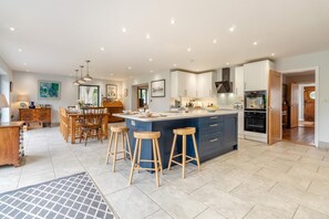 A modern kitchen with a central island, bar stools, and a dining area with wooden furniture. - 5 Bed in Walberswick (oc-hlodg2) (Walberswick)