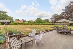 Une terrasse avec une table et des chaises, un jardin fleuri et une vue sur les environs.