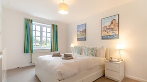Ein Schlafzimmer mit einem Bett, zwei Nachttischen, einem Fenster mit Vorhängen und zwei an der Wand befestigten Bildern.