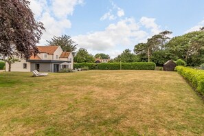 Une maison avec une pelouse, un abri de jardin et un arbre.