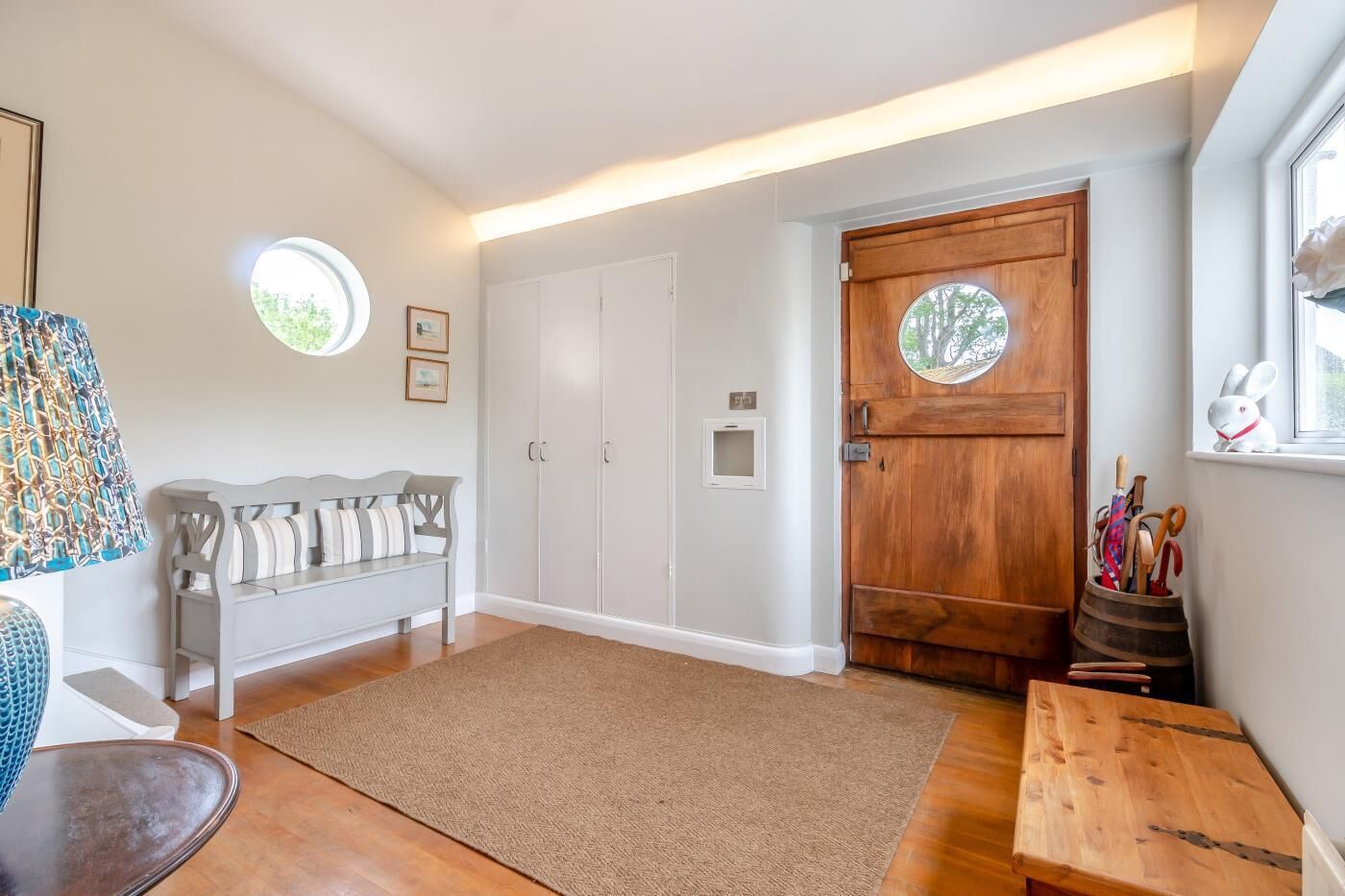 A room with a wooden door, a bench, a small table, and a window with a view.