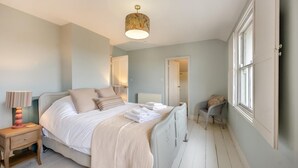 Et soveværelse med seng, natbord, lampe og stol.