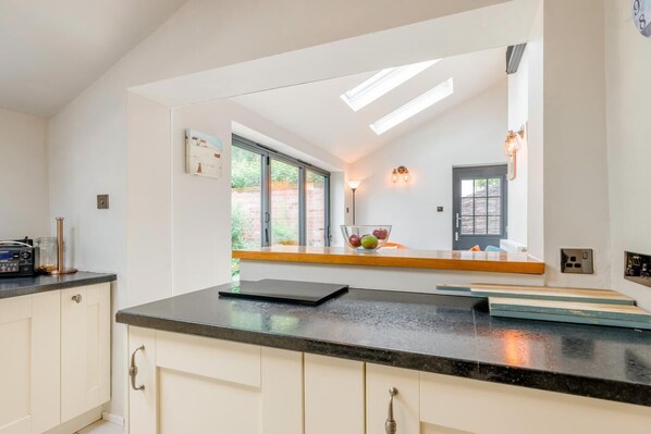 A modern kitchen with a black countertop, white cabinets, a window with a view, and a built-in oven. - 3 Bed in Wangford (oc-hchurc) (Wangford)