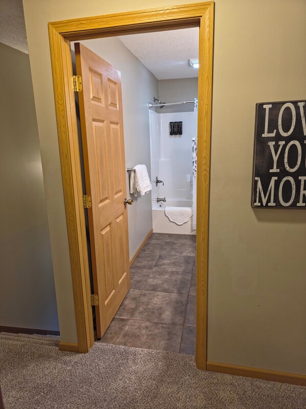 A hallway leading to a bathroom with a shower, a towel rack, and a sign that says "LOVE YOU MORE".