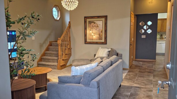 A modern living room with a grey sofa, wooden coffee table, and a chandelier. A staircase leads to another room, and a framed picture hangs on the wall. - Modern with traditional style 3-bed+ condo, wifi laundry in charming Laurel Oaks (Lima)