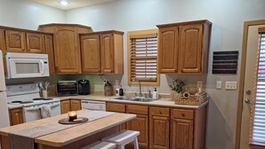 A kitchen with wooden cabinets, a microwave, a stove, a sink, and a bar area with stools. - Modern with traditional style 3-bed+ condo, wifi laundry in charming Laurel Oaks (Lima)