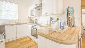 Eine moderne Küche mit weißen Schränken, einer Holzausziehtheke, einem eingebauten Backofen und einem Fenster mit Jalousien.