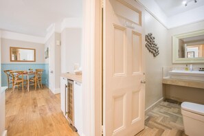 Una habitación con piso de madera, una mesa de comedor con sillas, una zona de cocina con un lavamanos y una puerta que dice 'Ruth'.