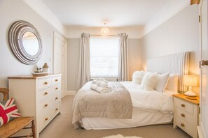 Un dormitorio con cama, mesitas de noche, cómoda, espejo y ventana con cortinas.