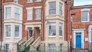 A row of red brick townhouses with bay windows, a blue door, and a green metal fence. - 2 Bed in Southwold (oc-hbrea) (Southwold)
