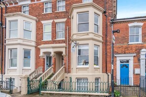 A row of red brick townhouses with bay windows, a blue door, and a green metal fence. - 2 Bed in Southwold (oc-hbrea) (Southwold)
