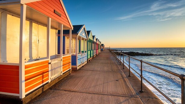 A seaside promenade with colorful beach huts and a wooden walkway. - 2 Bed in Southwold (oc-hbrea) (Southwold)