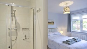 A hotel room with a glass-enclosed shower, a bed with neatly folded towels, a bedside lamp, and a window with a view of greenery. - 3 Bed in Reydon (oc-hspind) (Reydon)
