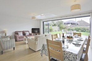 Een ruime woonkamer met een zithoek, een eettafel met stoelen en een televisie.