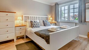 Ein Schlafzimmer mit einem großen Bett, einer weißen Kommode, Nachttischlampen und einem Fenster mit Vorhängen.