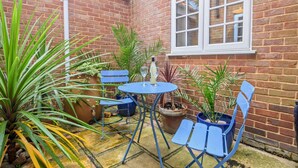 Eine Terrasse mit Tisch und Stühlen, umgeben von Kübelpflanzen und einer Ziegelmauer.