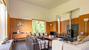 Een moderne woonkamer met een open haard, leren banken, een eethoek en een groot raam met uitzicht op groen.