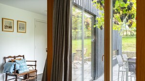Een kamer met een bed, een bankje en een grote schuifdeur die leidt naar een terras buiten met stoelen en een tafel.