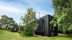 Een modern, zwart metalen gebouw met een plat dak, omringd door een verzorgd gazon en bomen.