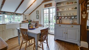 A rustic kitchen with wooden beams, a large window, and a white cabinet with tea mugs. - 4 Bed in Wrentham (oc-hdress) (Wrentham)