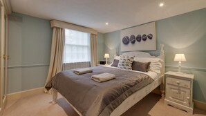 A bedroom with a large bed, two bedside tables, a window with curtains, and a wall art piece. - 4 Bed in Wrentham (oc-hdress) (Wrentham)