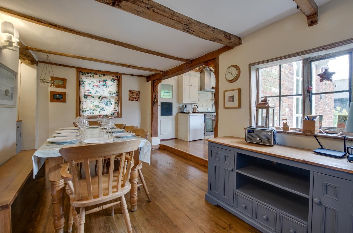 A dining area with a wooden table set for six, a kitchen with white cabinets, and a window with a star decoration.