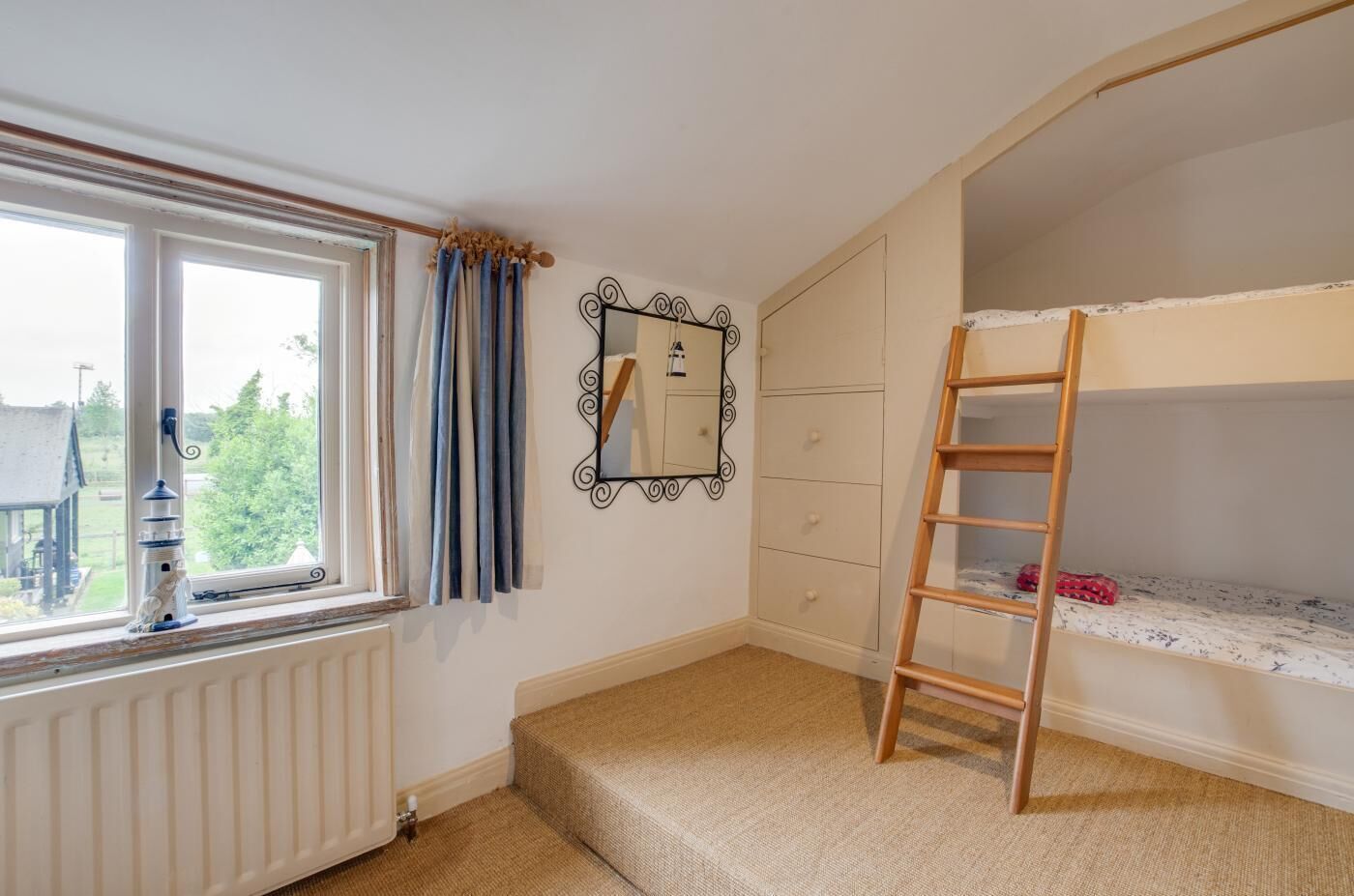 Une chambre avec un lit superposé, un radiateur, une fenêtre avec des rideaux, un miroir et une échelle.