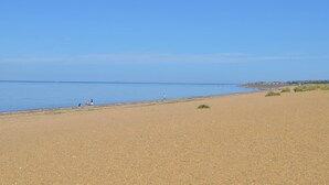 Een breed zandstrand met een heldere blauwe lucht en een kalme zee.