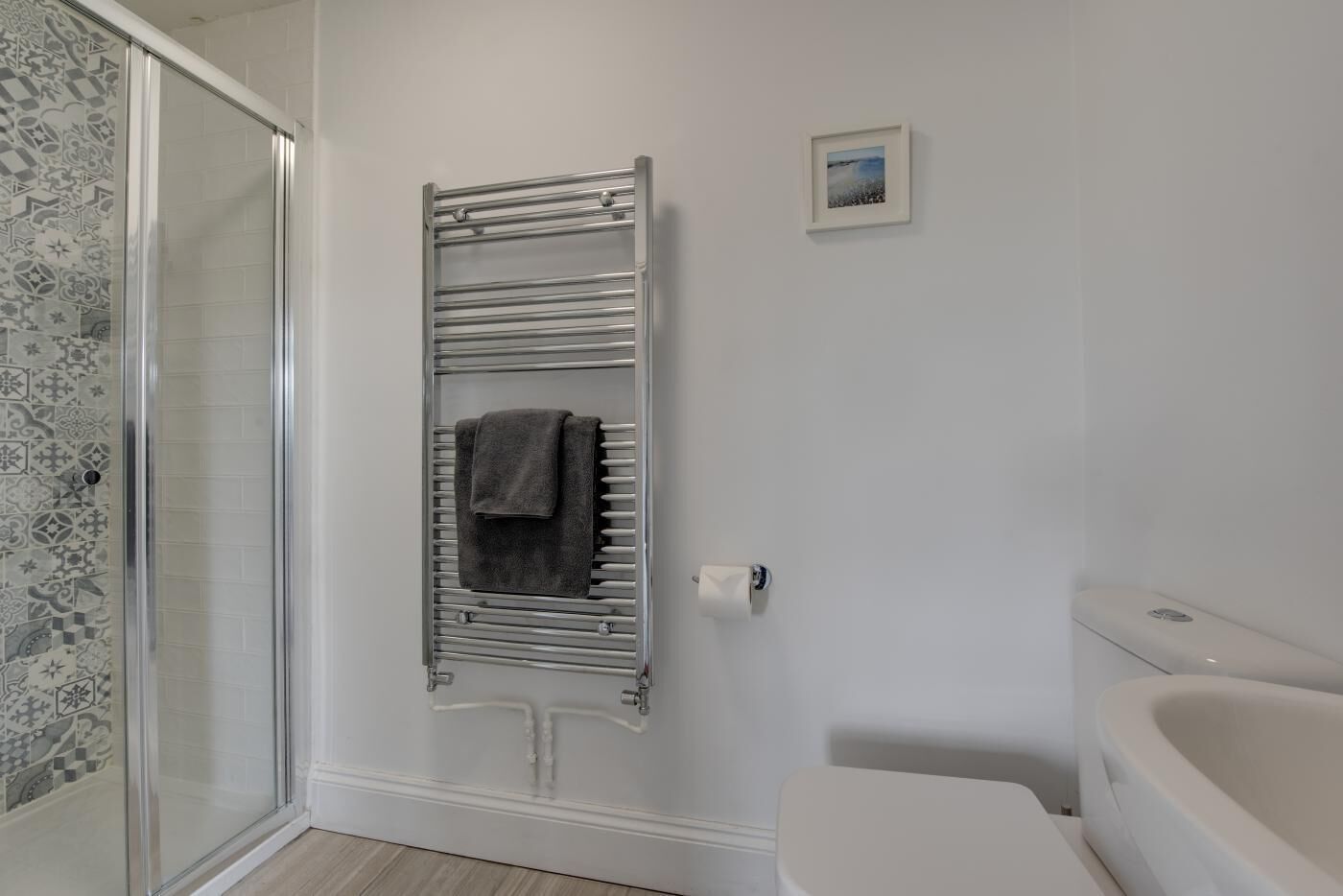 A bathroom with a glass shower enclosure, a towel rack with a towel, a toilet, and a small framed picture on the wall.