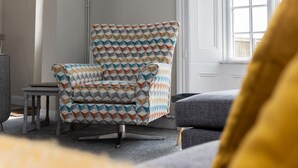 Een kamer met een fauteuil met patroon, een tafeltje en een bank.