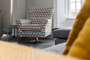 Una habitación con un sillón estampado, una mesita y un sofá.