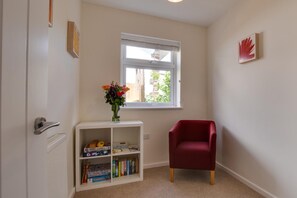Ein Zimmer mit Fenster, ein Bücherregal mit Spielen, ein roter Sessel und eine Vase mit Blumen.