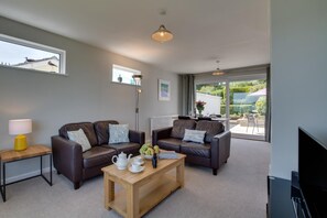 Ein modernes Wohnzimmer mit zwei Ledersofas, einem Holztisch, einem Fernseher und einem Essbereich mit Tisch und Stühlen.