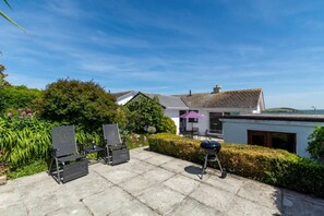 A patio with outdoor furniture, a barbecue grill, and a house with a white exterior and grey roof. - 2 Bed in Padstow (oc-p00738) (Padstow)