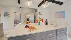 Cozinha moderna com ilha grande, armários brancos e uma viga de teto escura.
