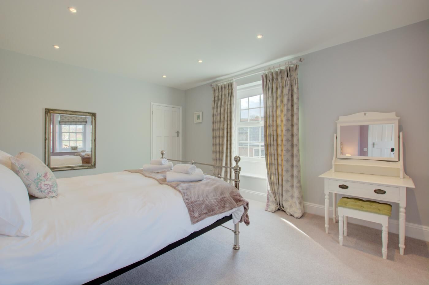 A bedroom with a large bed, a dresser, a mirror, and a window with curtains.