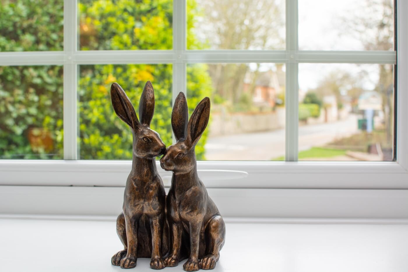 Two bronze rabbit figurines on a white windowsill.